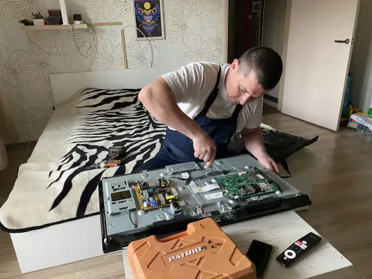Мастер разбирает телевизор на полу в квартире